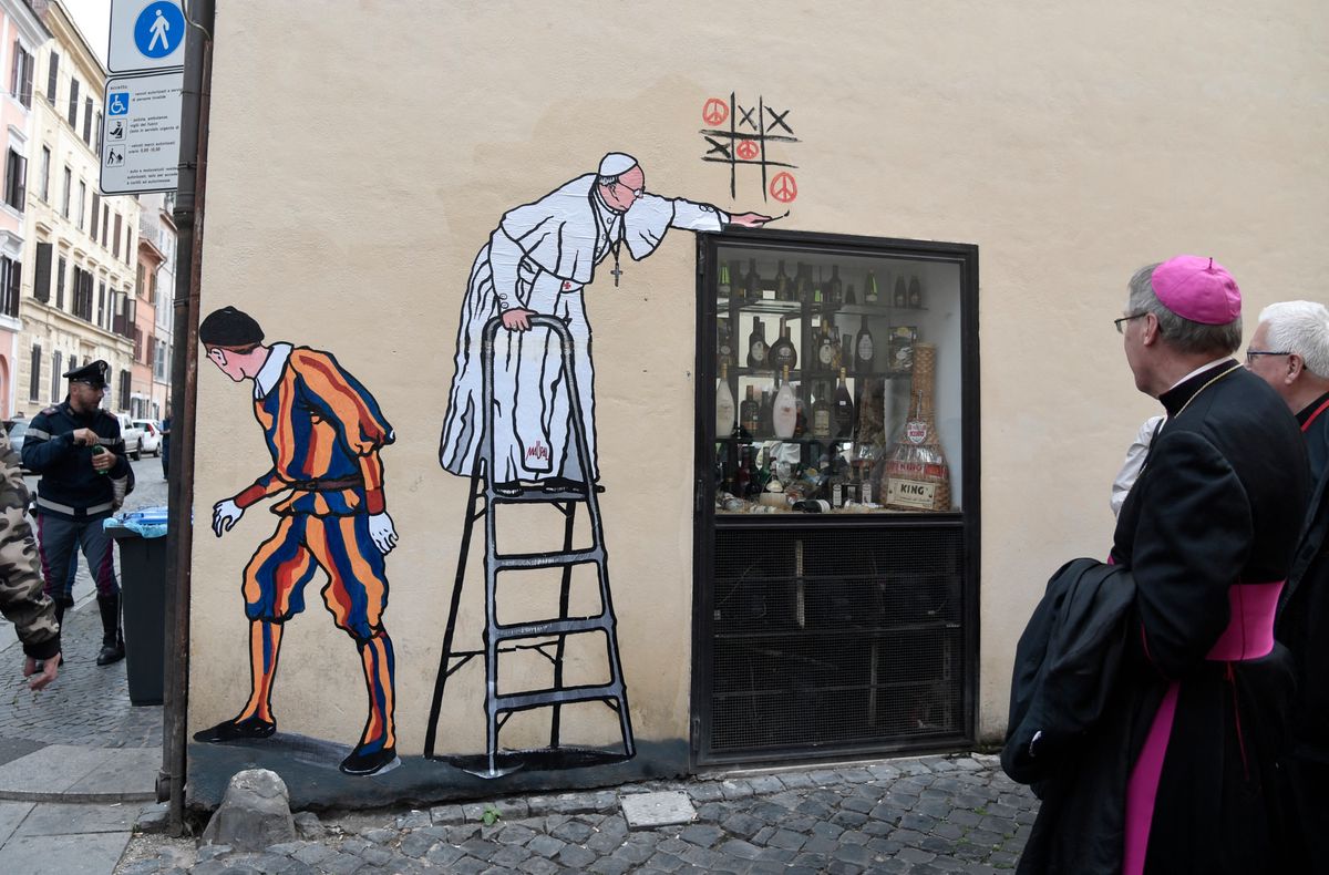 Un évêque passe devant un collage street-art de Maupal montrant le pape François jouant au morpion et dessinant des signes de paix, surveillé par un garde suisse près du Vatican, Rome, 19 octobre 2016.