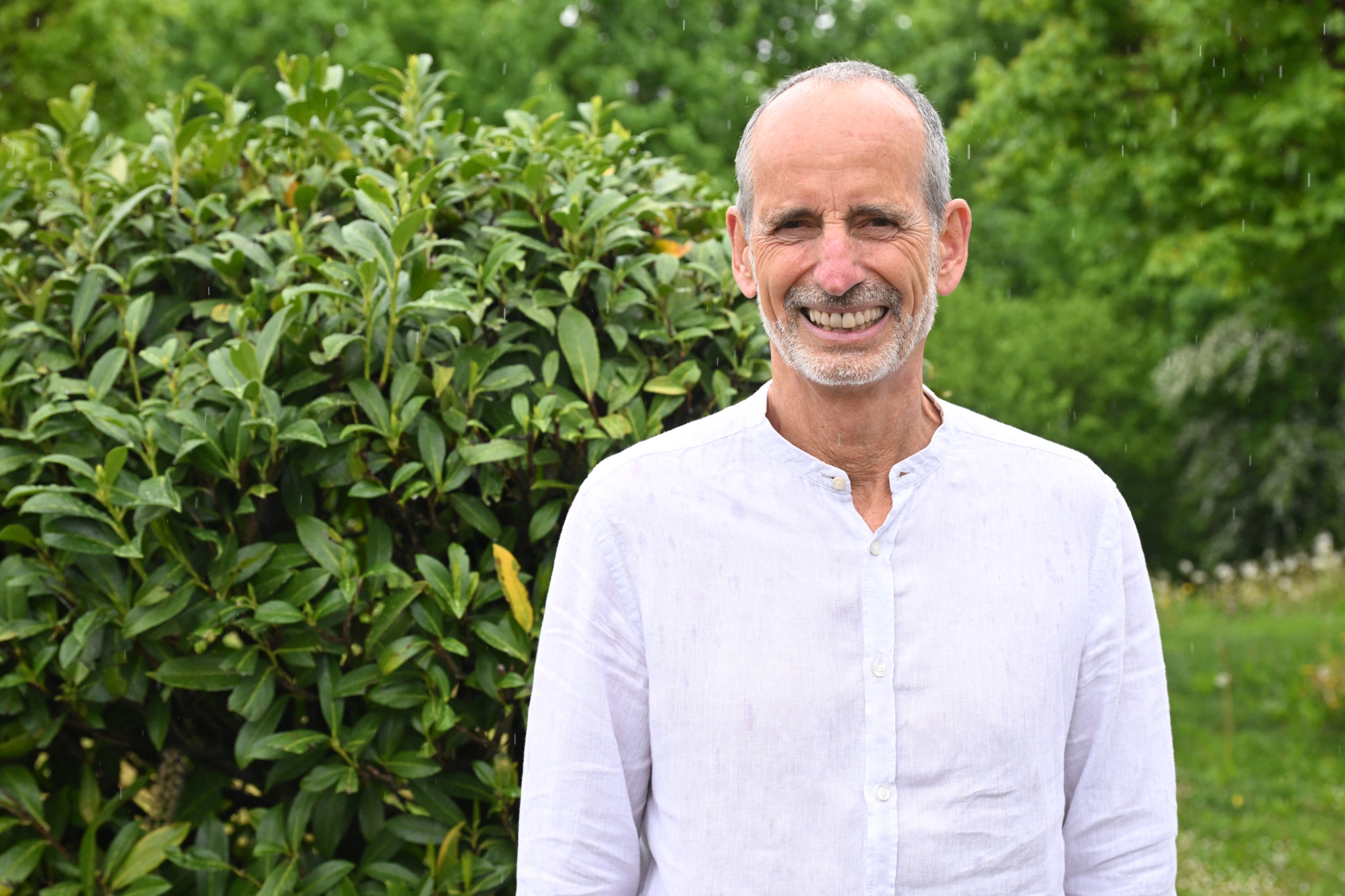 Roland Liebscher Bracht, expert en gestion de la douleur, souriant devant un buisson verdoyant.