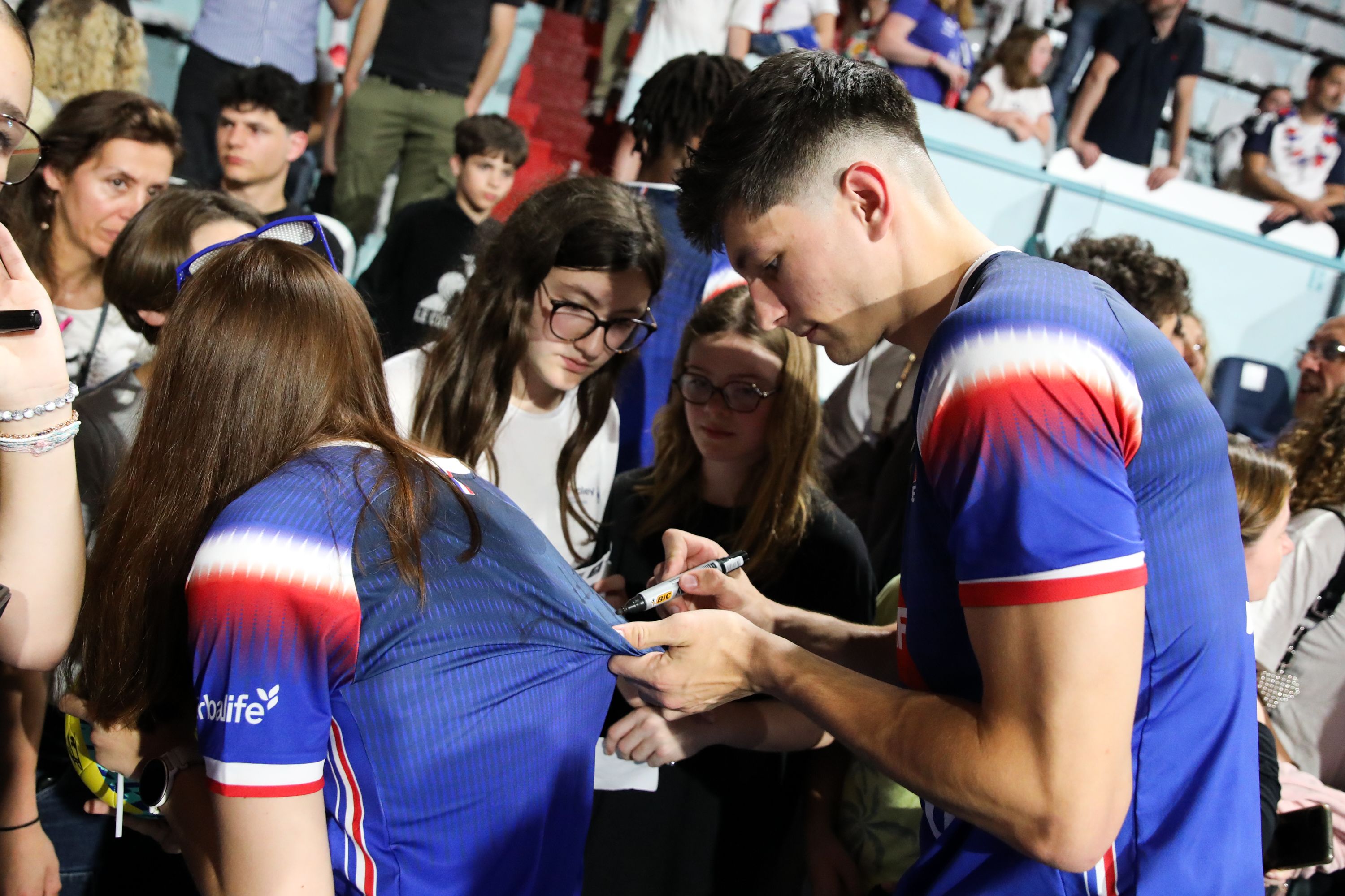 Nathan Feral dédicace un maillot de l’équipe de France porté par une supportrice lors de la rencontre des joueurs avec le public.