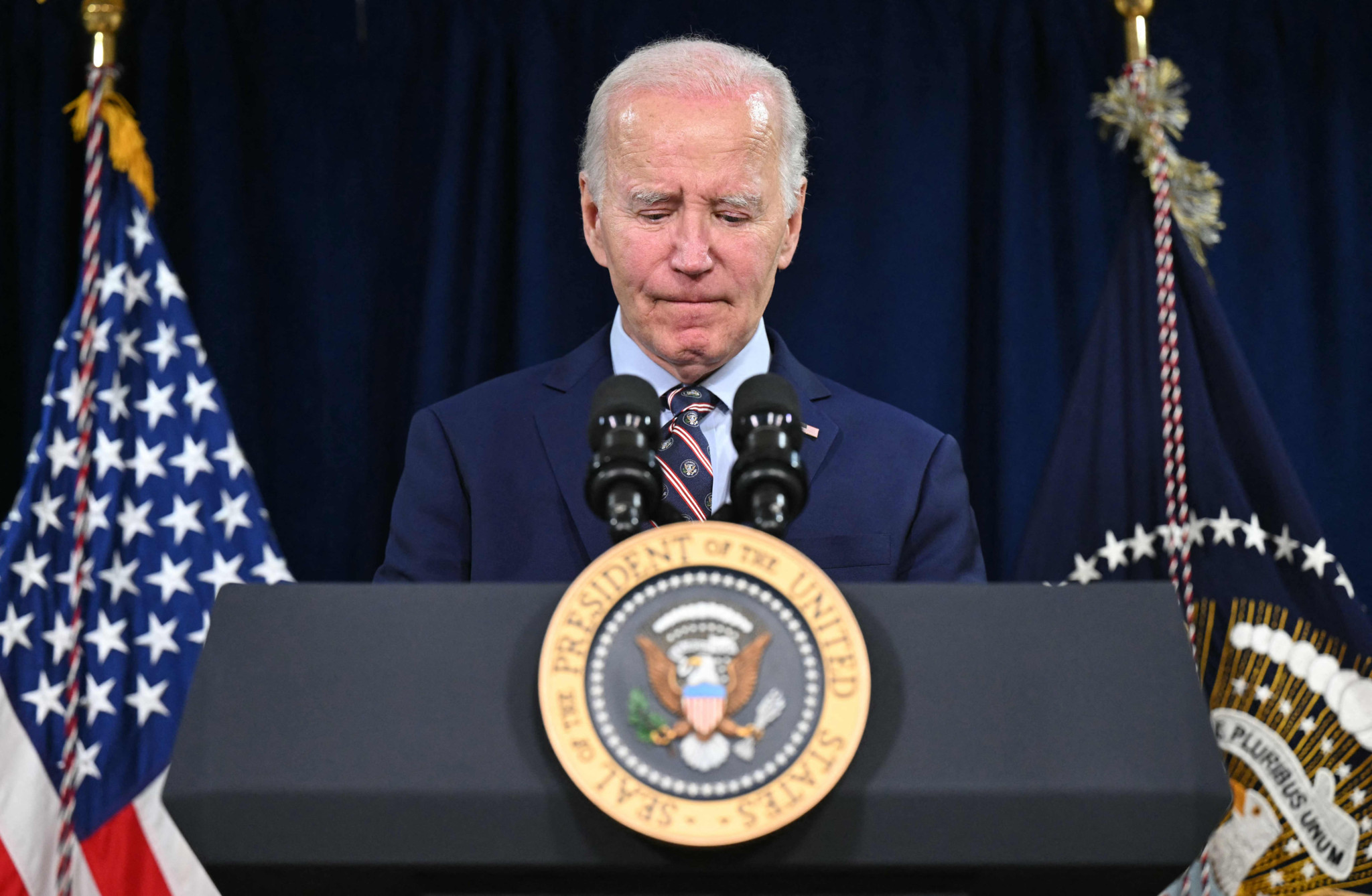Joe Biden, président des États-Unis, prononce un discours sur le décès de l’ancien président Jimmy Carter à Christiansted, Saint-Croix, avec un sceau présidentiel en avant-plan. Drapeaux américains et sceau présidentiel en arrière-plan.