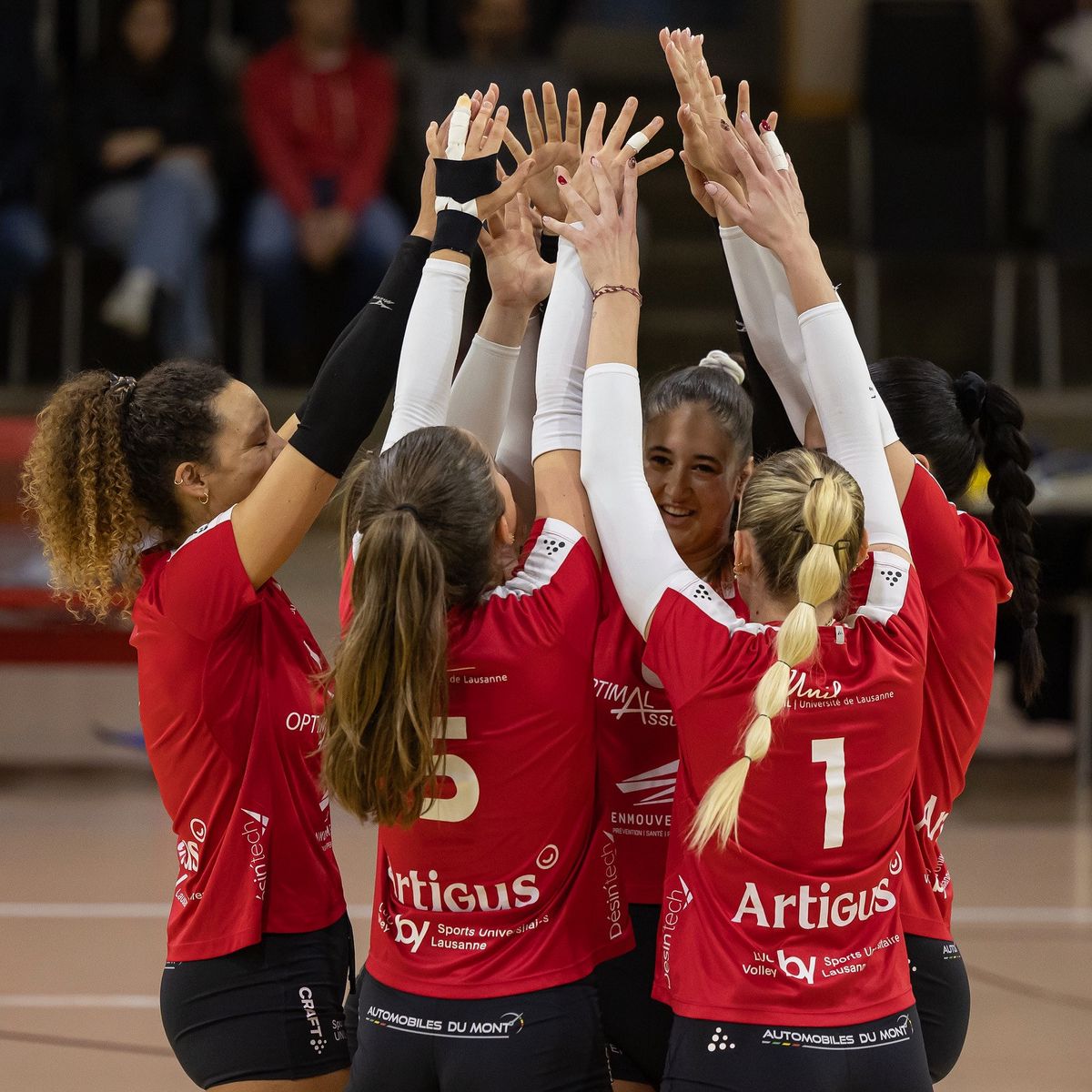 Joueuses de volley-ball en rouge se congratulent au centre d’un terrain en intérieur.