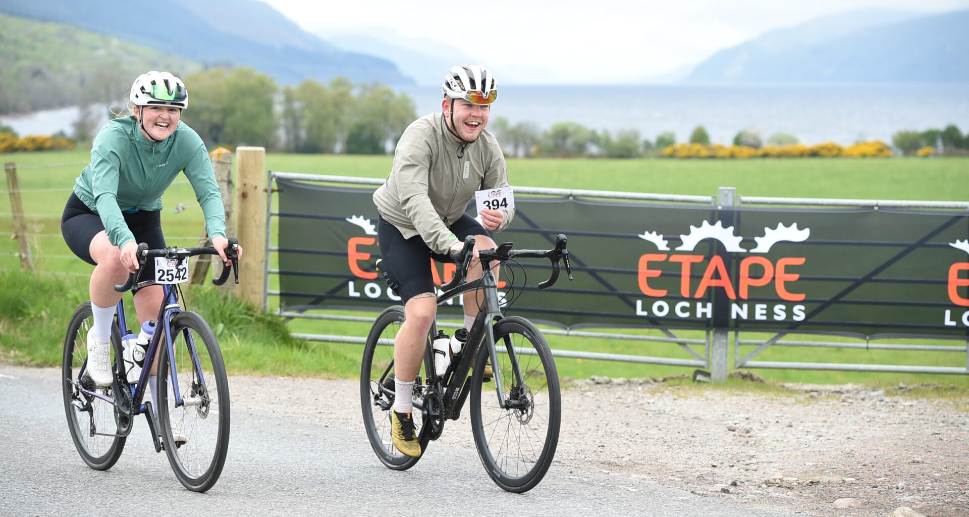 Adam Becket in a beige jacket rides along next to Katherine Moore in a
