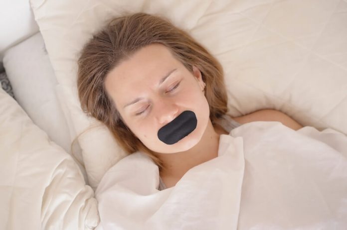 Mouth Taping dormir ruban bouche respiration dangers ma sante Une jeune femme dormant avec un ruban sur la bouche.