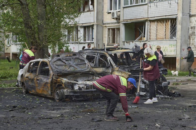 Des employés municipaux nettoient les alentours de voitures brûlées dans le quartier résidentiel après l'attaque de drone russe à Kiev, en Ukraine, le dimanche 4 mai 2025.