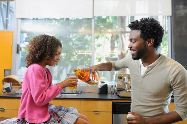 Un père sert du jus de pomme à sa fille.