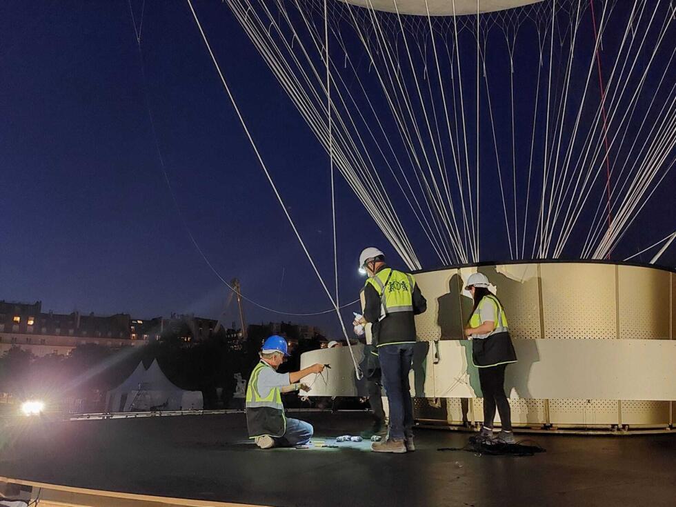 Des ouvriers s'affairent autour des cordages de la vasque olympique. Ce soir-là, trois tests de levage sont réalisés avec et sans la flamme, pour être fin prêt ce samedi 21 juin.