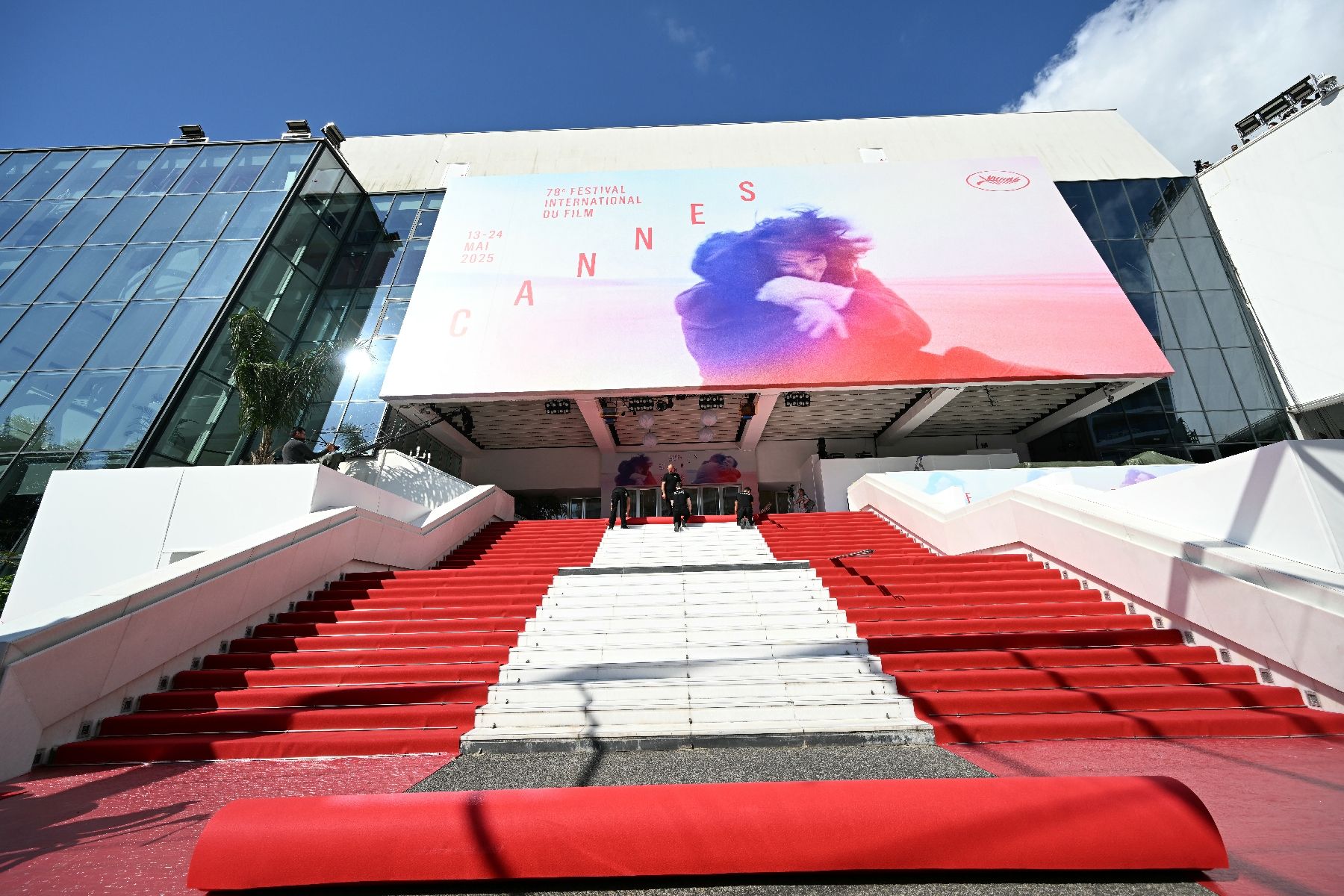 Des employés déroulent le tapis rouge sur les marches du palais des Festivals pour le Festival de Cannes le 13 mai 2025, dans les Alpes-Maritimes