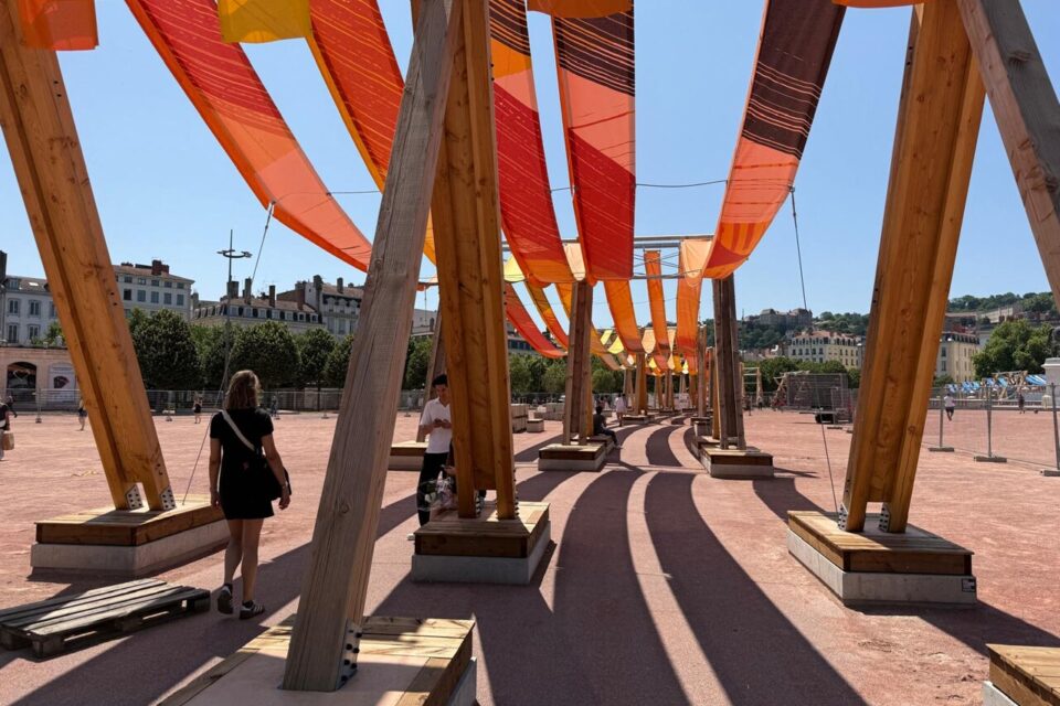 Des passants en-dessous d'une partie de l'œuvre Tissages urbains place Bellecour.