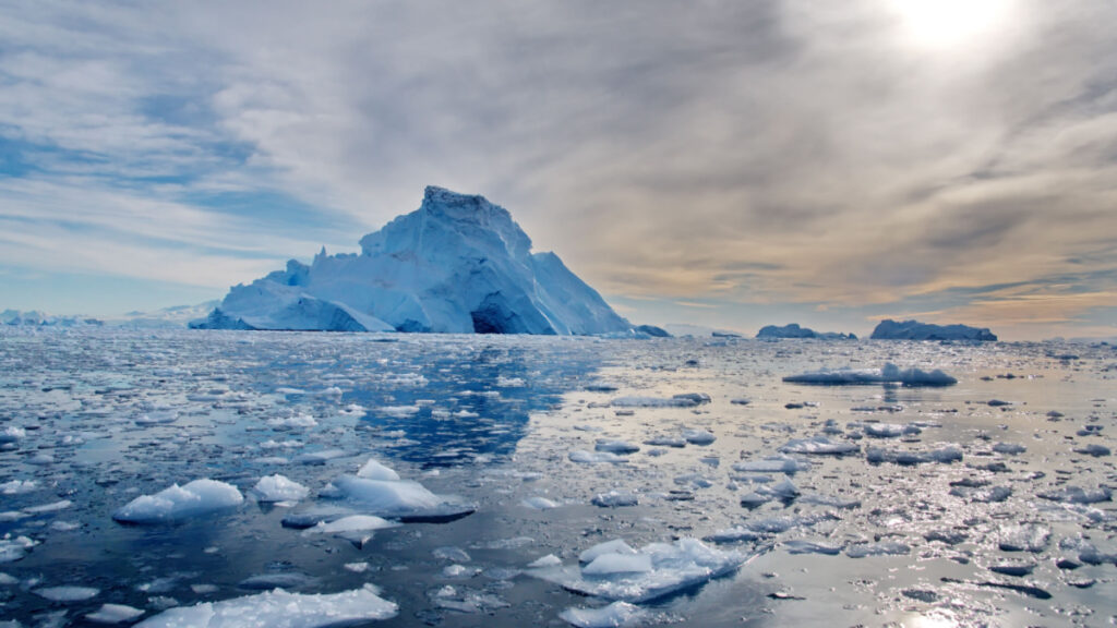 Iceberg monumental et fragments de glace flottant sur une mer partiellement dégelée en Antarctique sous un ciel voilé