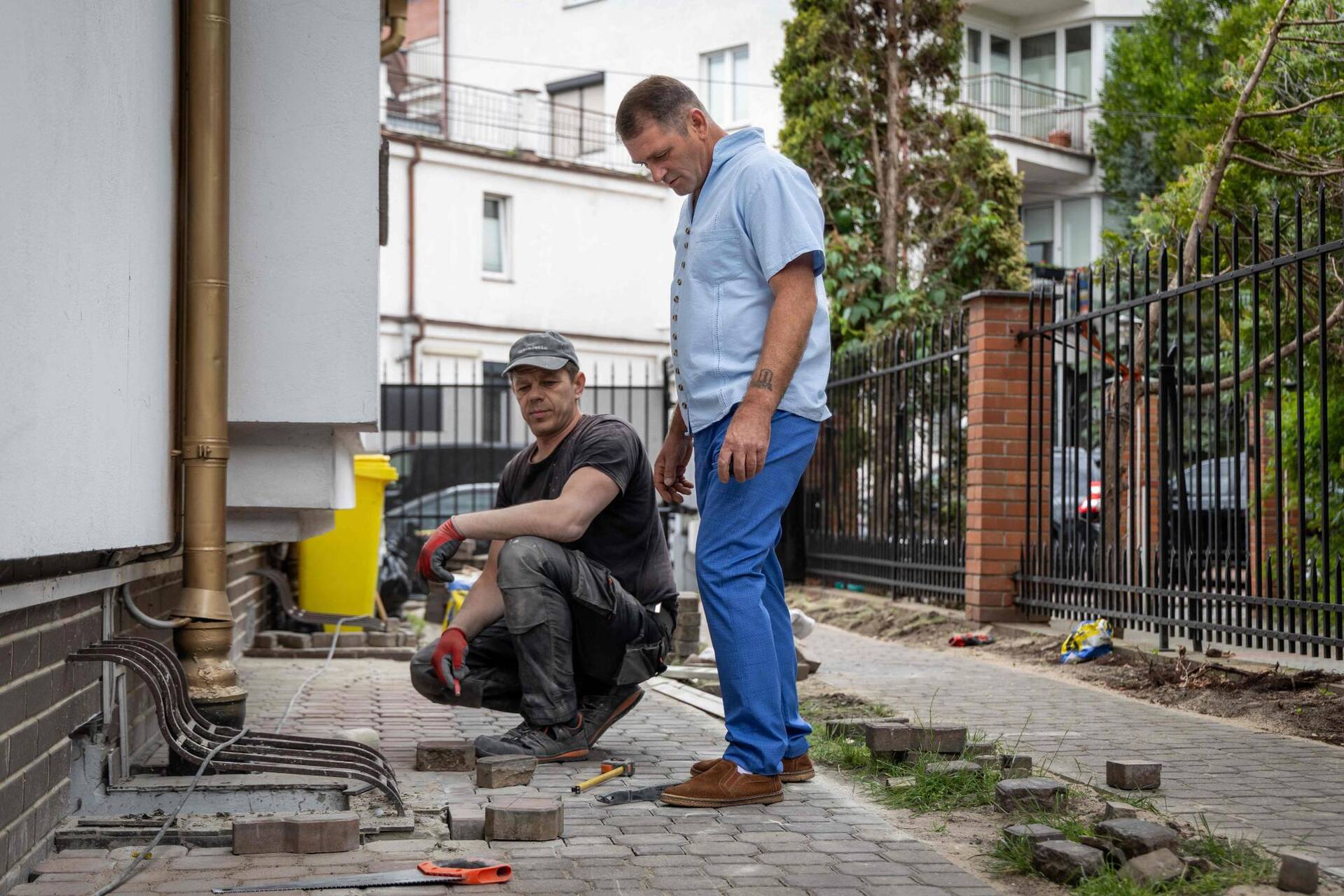 Vitalii Vizinskyi (à droite), propriétaire d'une entreprise de construction ukrainienne, supervise le travail de ses employés qui posent des pavés dans le jardin d'une ambassade à Varsovie, le 24 juin 2025. — © WOJTEK RADWANSKI / AFP