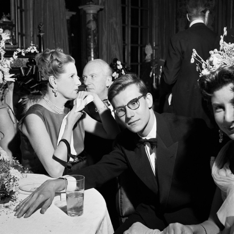 Un groupe de personnes élégamment vêtues assises autour d’une table lors d’un événement, avec des décorations florales.