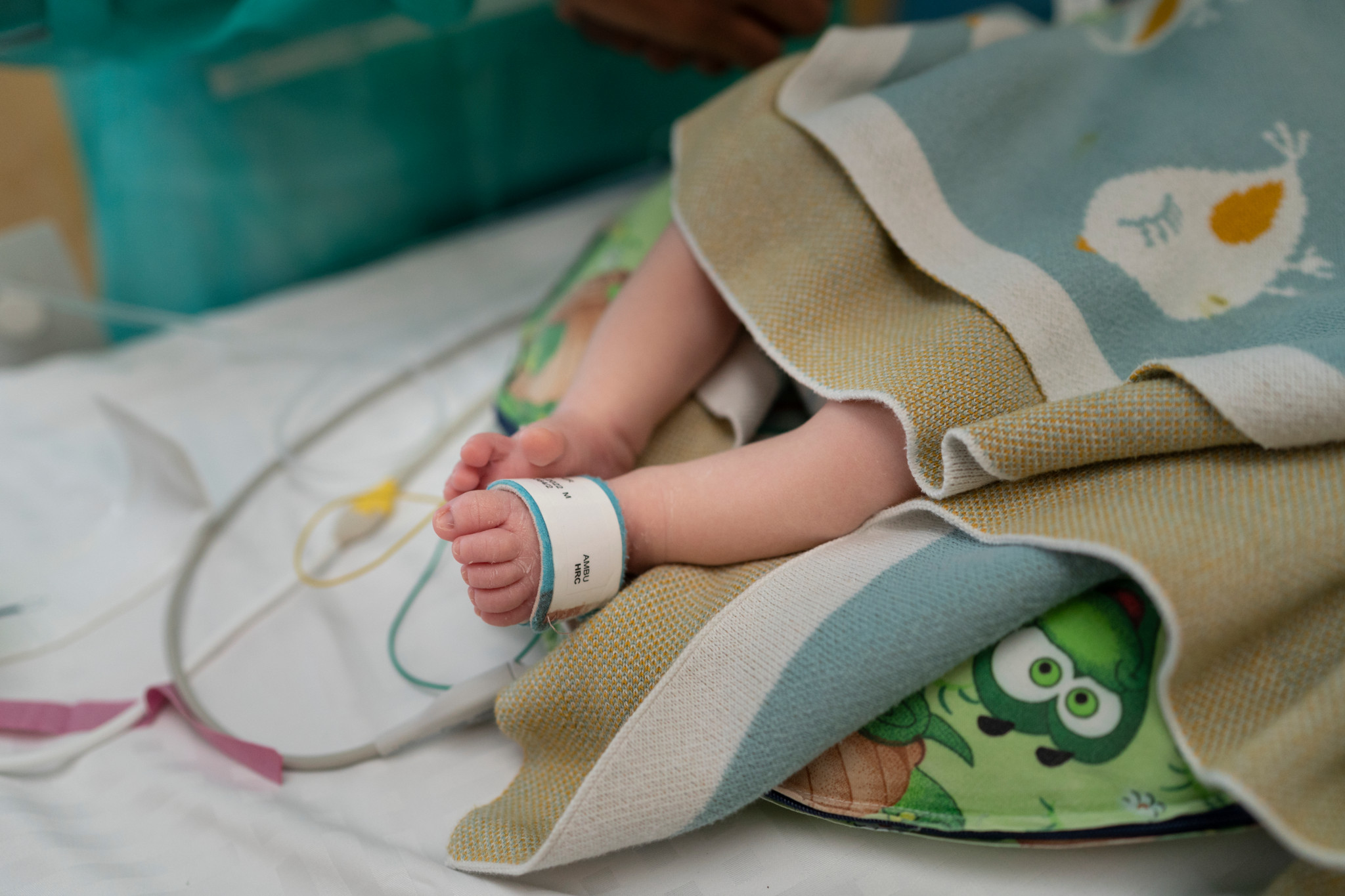 Bébé prématuré soigné dans le service de néonatologie du CHUV à Lausanne, couvert d’une couverture avec un bracelet d’identification.