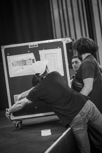 Espace Django 2025, coulisses, rangement, musiciens, techniciens, concert, salle, malles, ambiance, montage