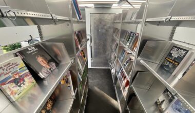 L'intérieur d'une fourgonnette, aménagée avec des étagères en métal où sont présentés des livres.