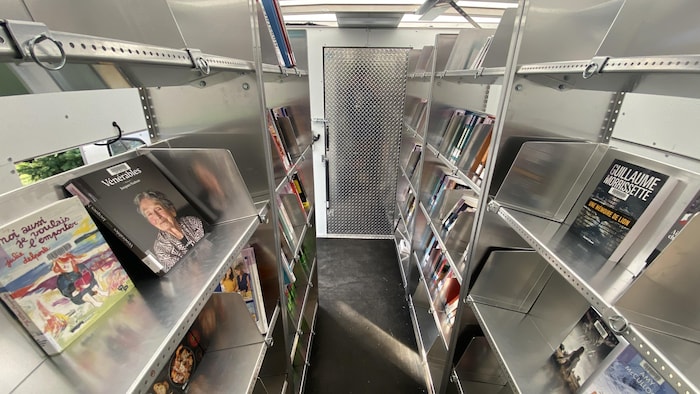 L'intérieur d'une fourgonnette, aménagée avec des étagères en métal où sont présentés des livres.
