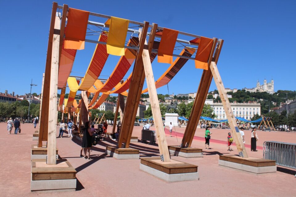 Des passants s'arrêtent et s'installent sous l'œuvre Tissage urbain, place Bellecour, à Lyon, mercredi 9 juillet.