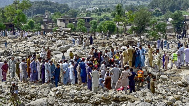 Des habitants observent les secouristes retirer les pierres devant leurs maisons au lendemain des crues soudaines survenues dans le district de Buner, au nord du Pakistan, le 16 août 2025. (HASHAM AHMED / AFP)
