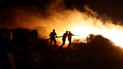 Des pompiers luttent contre le feu près de Keratea, au sud-est d'Athènes, en Grèce, le 8 août 2025. (COSTAS BALTAS / ANADOLU / AFP)