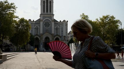 Une femme tente de se rafraîchir à l'aide d'un éventail dans les rues de Saint-Etienne (Loire), le 12 août 2025. (MATHIEU PRUDHOMME / ANADOLU VIA AFP)