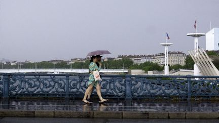 Deux personnes sous la pluie, pont de l'Université à Lyon, le 3 mai 2025. (ELSANA ADZEMOVIC / HANS LUCAS / AFP)
