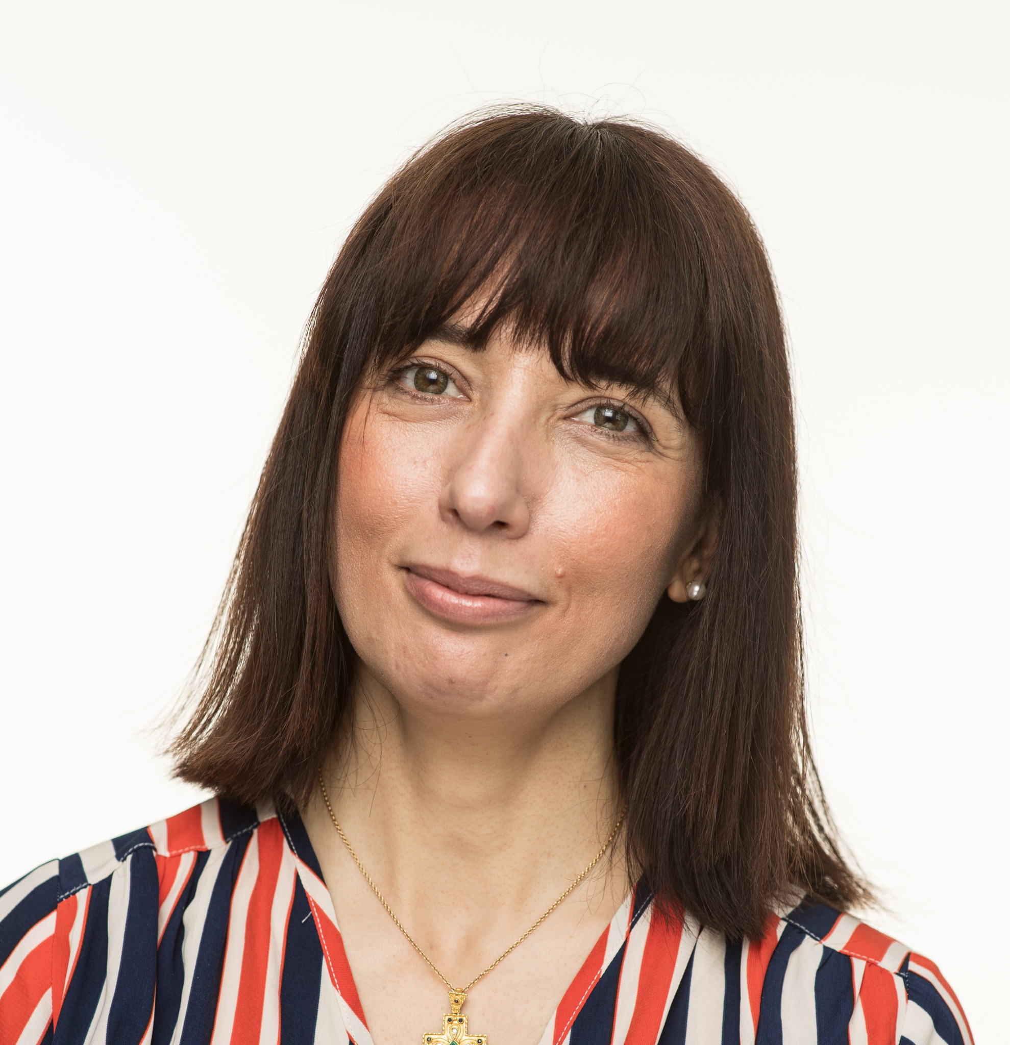Une femme aux cheveux bruns et raides portant une chemise rayée rouge et bleue, souriant légèrement.