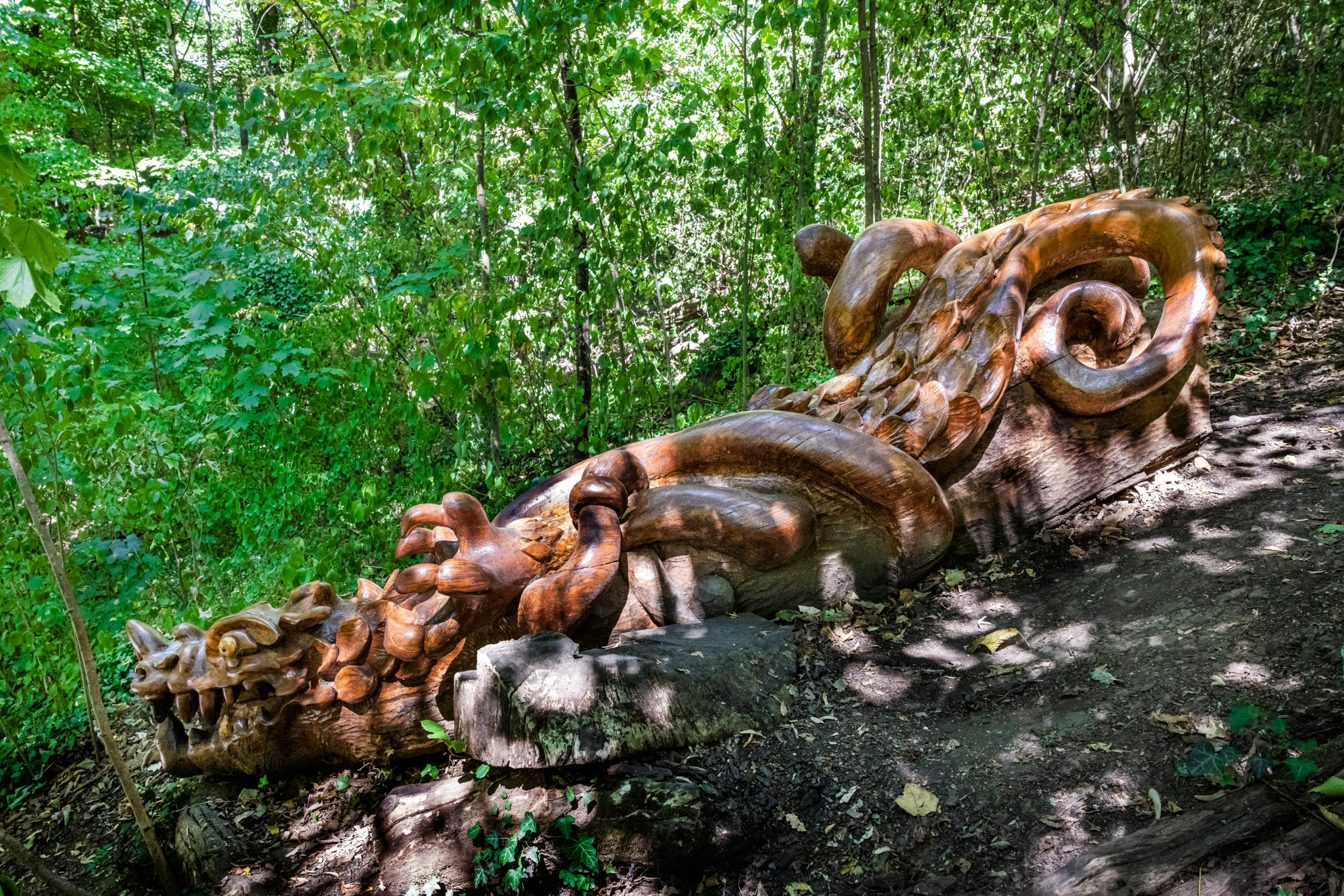 Sculpture en bois représentant un dragon dans la campagne Masset à Saint-Jean, réalisée par Jacques Baume, entourée de végétation verdoyante.
