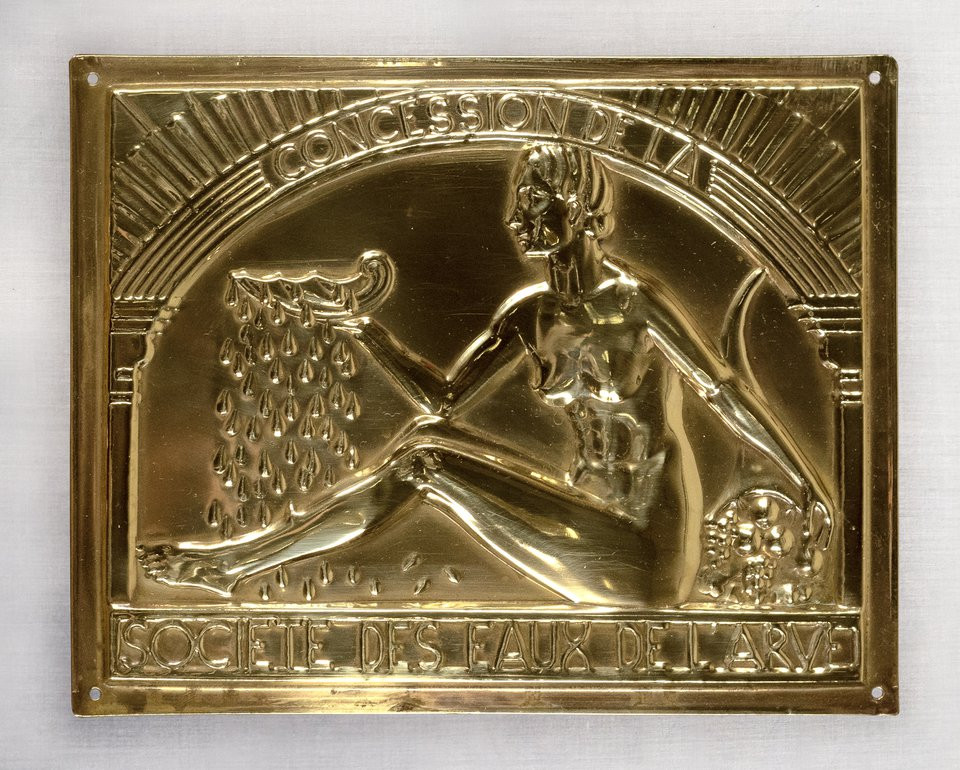 Plaque dorée représentant une figure allégorique versant de l’eau, avec l’inscription "CONCESSION DE LA SOCIÉTÉ DES EAUX DE LARV".