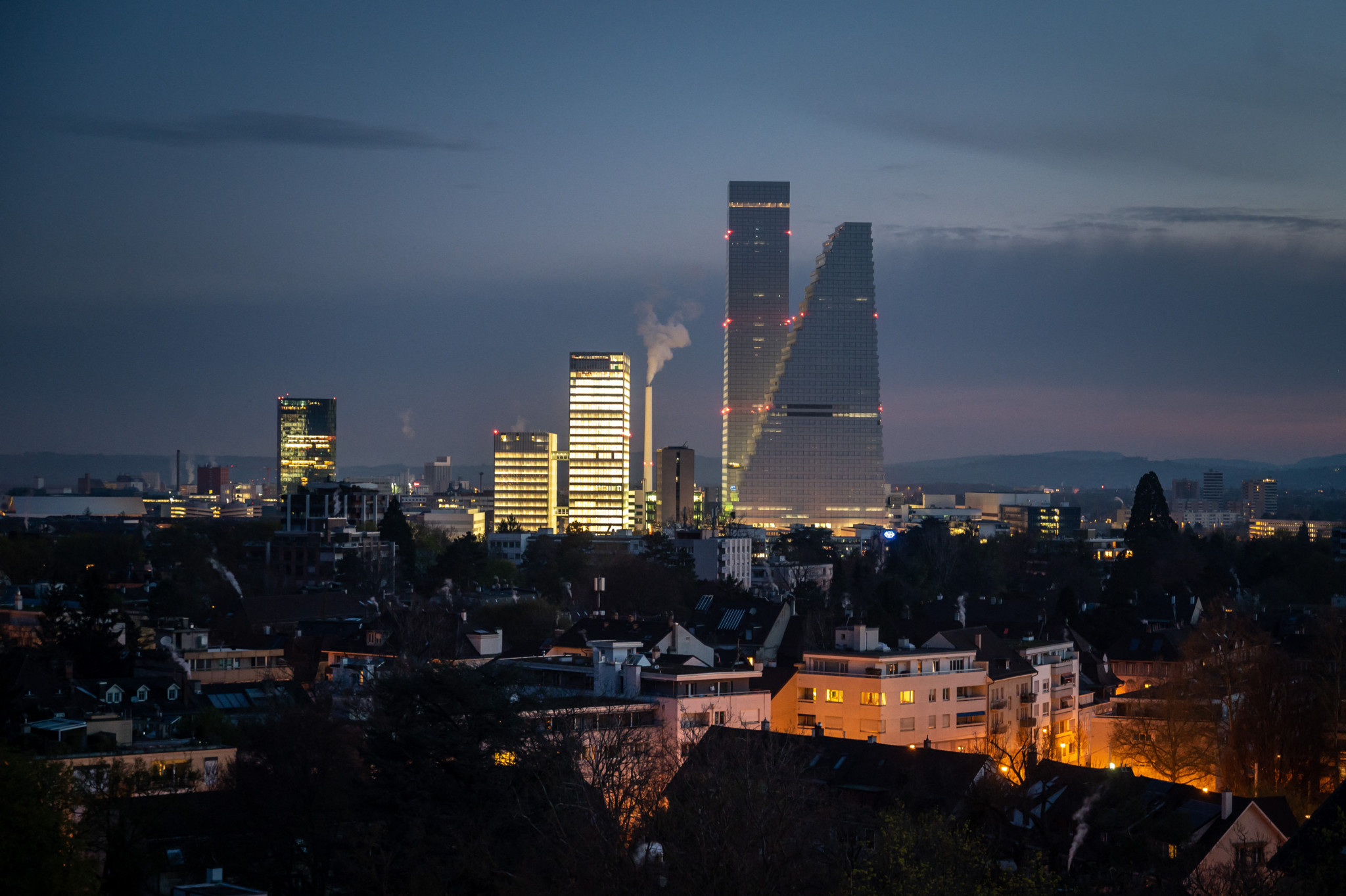 Vue nocturne des deux tours Roche à Bâle, conçues par les architectes Herzog et de Meuron, éclairées avec d’autres bâtiments environnants.