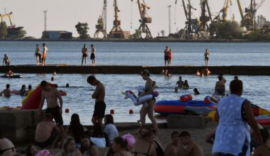 Des estivants profitent de la plage à Marioupol, citée ukrainienne contrôlée par la Russie, avec le port de commerce à l'arrière-plan, le 14 juillet 2025