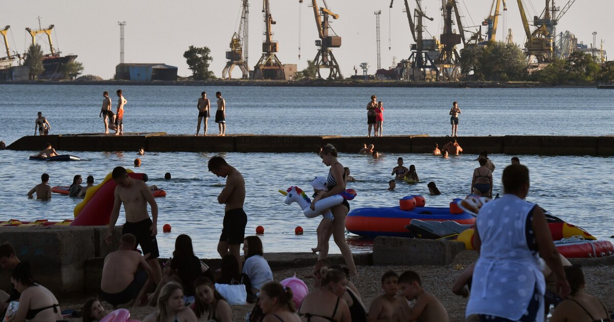 Des estivants profitent de la plage à Marioupol, citée ukrainienne contrôlée par la Russie, avec le port de commerce à l'arrière-plan, le 14 juillet 2025