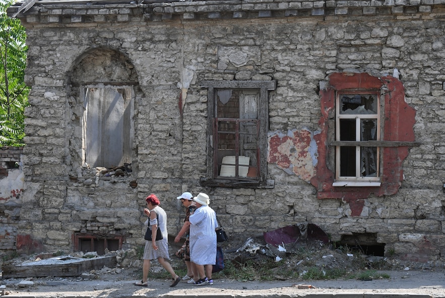 Des femmes passent devant une maison détruit par les combats, dans la ville ukrainienne de Marioupol contrôlée par la Russie, le 16 juillet 2025