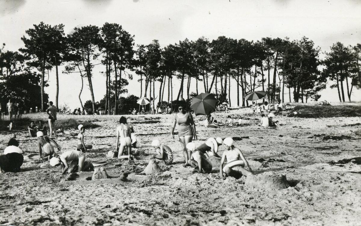Tenues et bonnets de bain caractéristiques de l’époque. Parasols et pâtés de sable et immuables