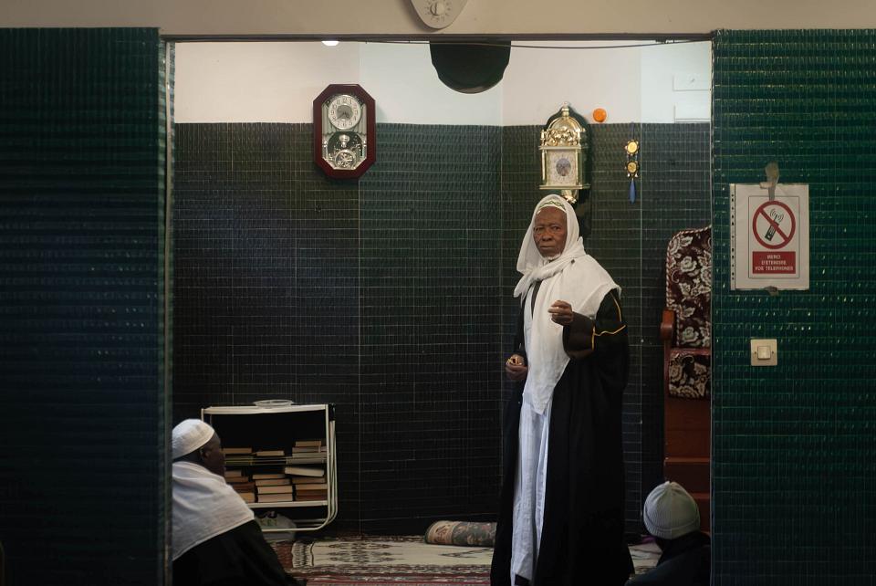Un veil homme est debout et deux homme assis devant lui. 