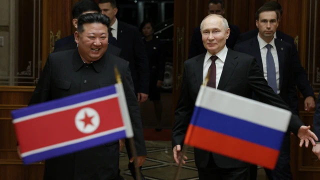 Kim Jong Un (à gauche) sourit alors qu'il marche aux côtés de Vladimir Poutine (à droite) devant les drapeaux nationaux de la Corée du Nord et de la Russie.