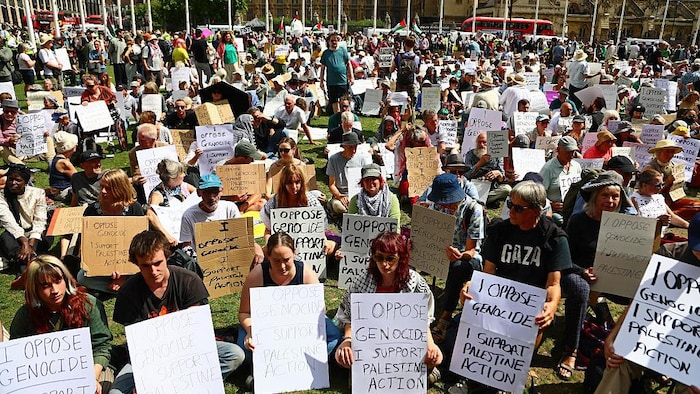 Des manifestants assis au sol avec des pancartes où on peut lire des slogans sympathisants à la Palestine.