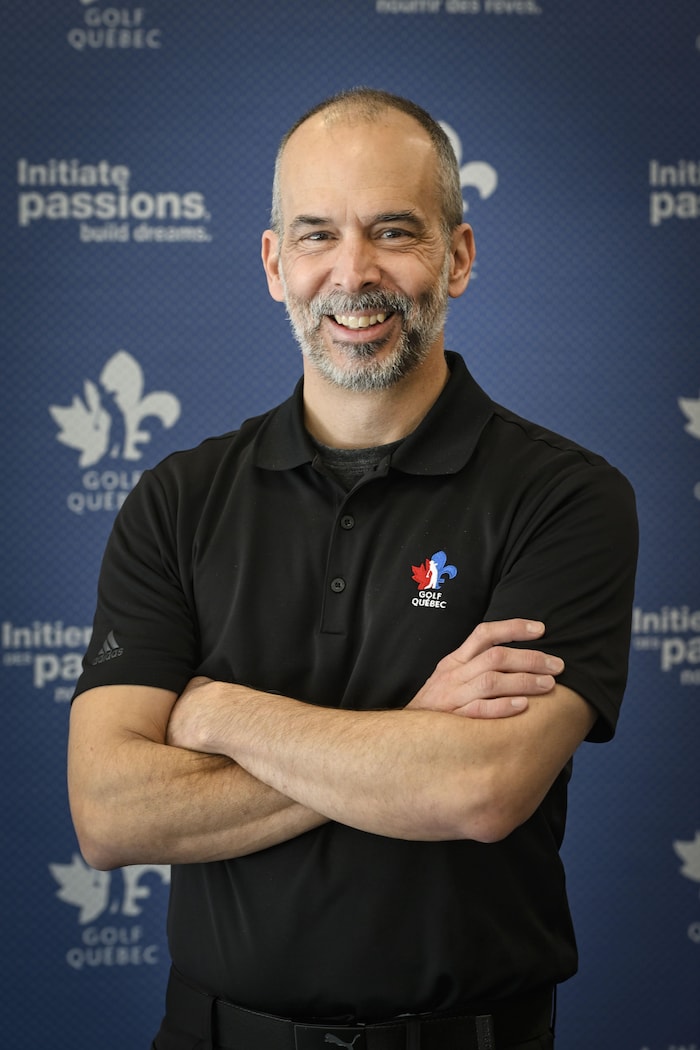 Un homme en noir, sourit, les bras croisés.