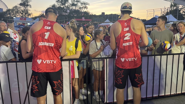 Deux hommes sont attendus par une foule derrière une barrière.
