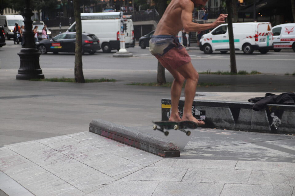 Torse nu, un skateur s'essaie à une figure sur le diamant central de la place de la République. 