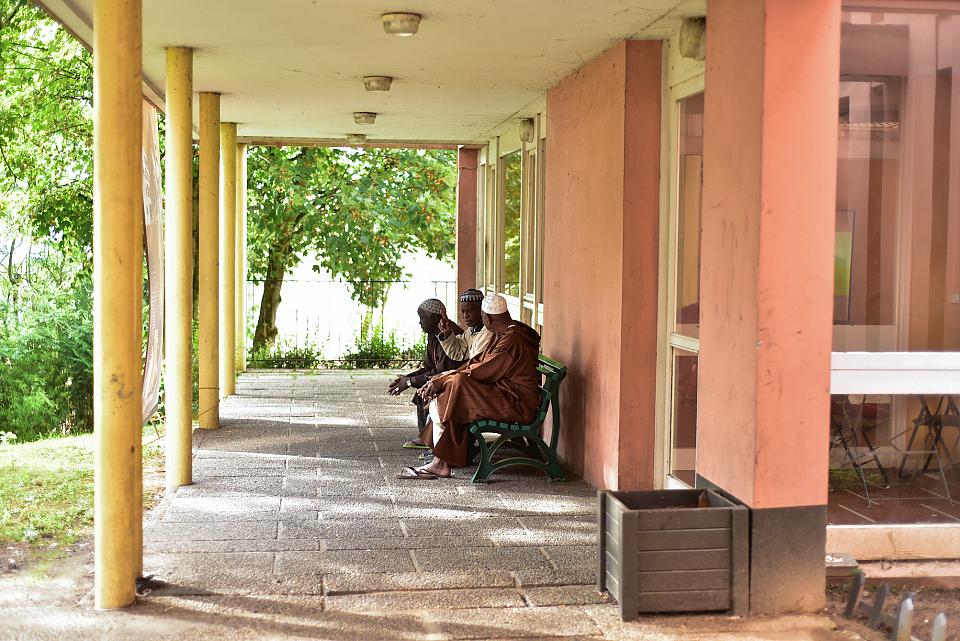 Trois hommes discutent assis sur un banc à l'extérieur.
