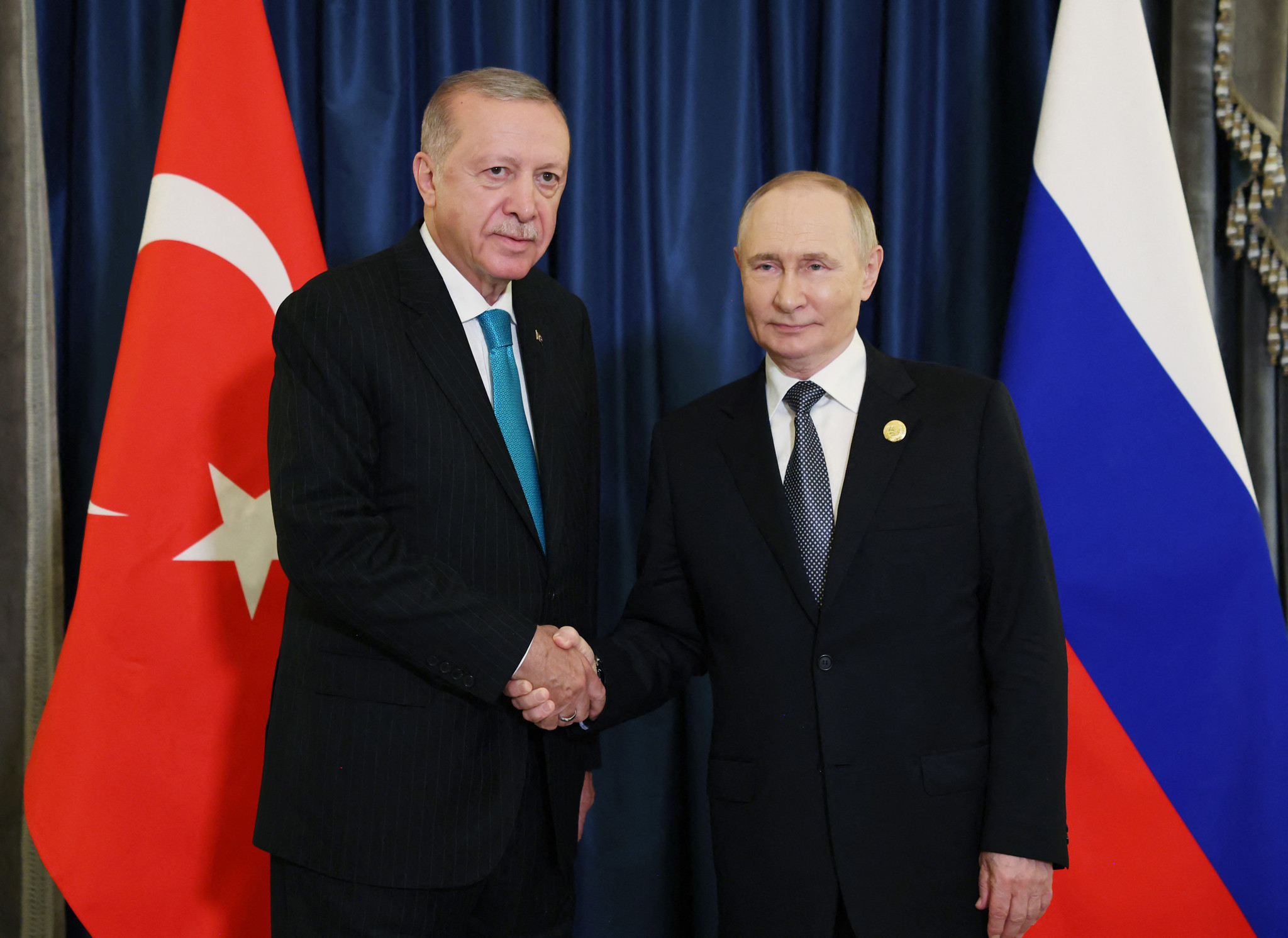 Le président turc Recep Tayyip Erdogan serre la main du président russe Vladimir Poutine lors du 25e sommet de l’Organisation de coopération de Shanghai à Tianjin, avec les drapeaux turc et russe en arrière-plan.