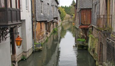 Un canal étroit coule entre de vieux bâtiments avec des lanternes et de la verdure, créant une scène pittoresque.