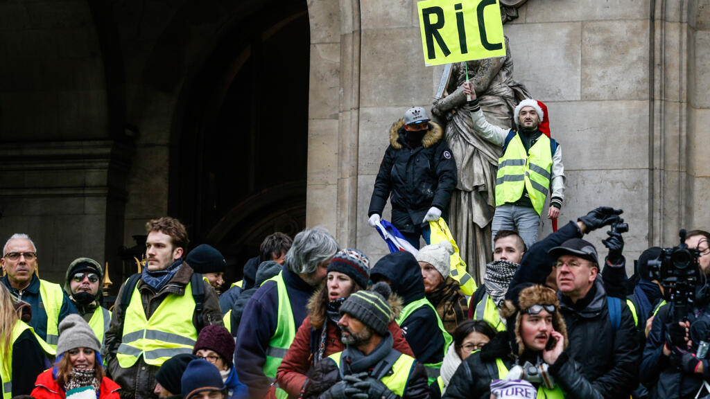 Un gilet jaune tient un carton portant l'inscription «référendum d’initiative citoyenne  - RIC» lors d'une manifestation contre la hausse du coût de la vie, devant l'Opéra de Paris, le 15 décembre 2018. 