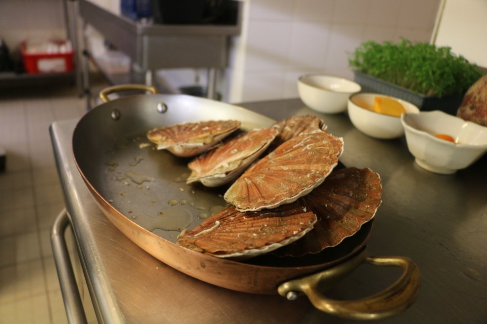 La première étape consiste à ouvrir les coquilles Saint-Jacques. Pour éviter le gaspillage, on récupère les bardes qu'on ajoutera ensuite dans la sauce pour apporter du goût. Il faudra bien rincer la Saint-Jacques.