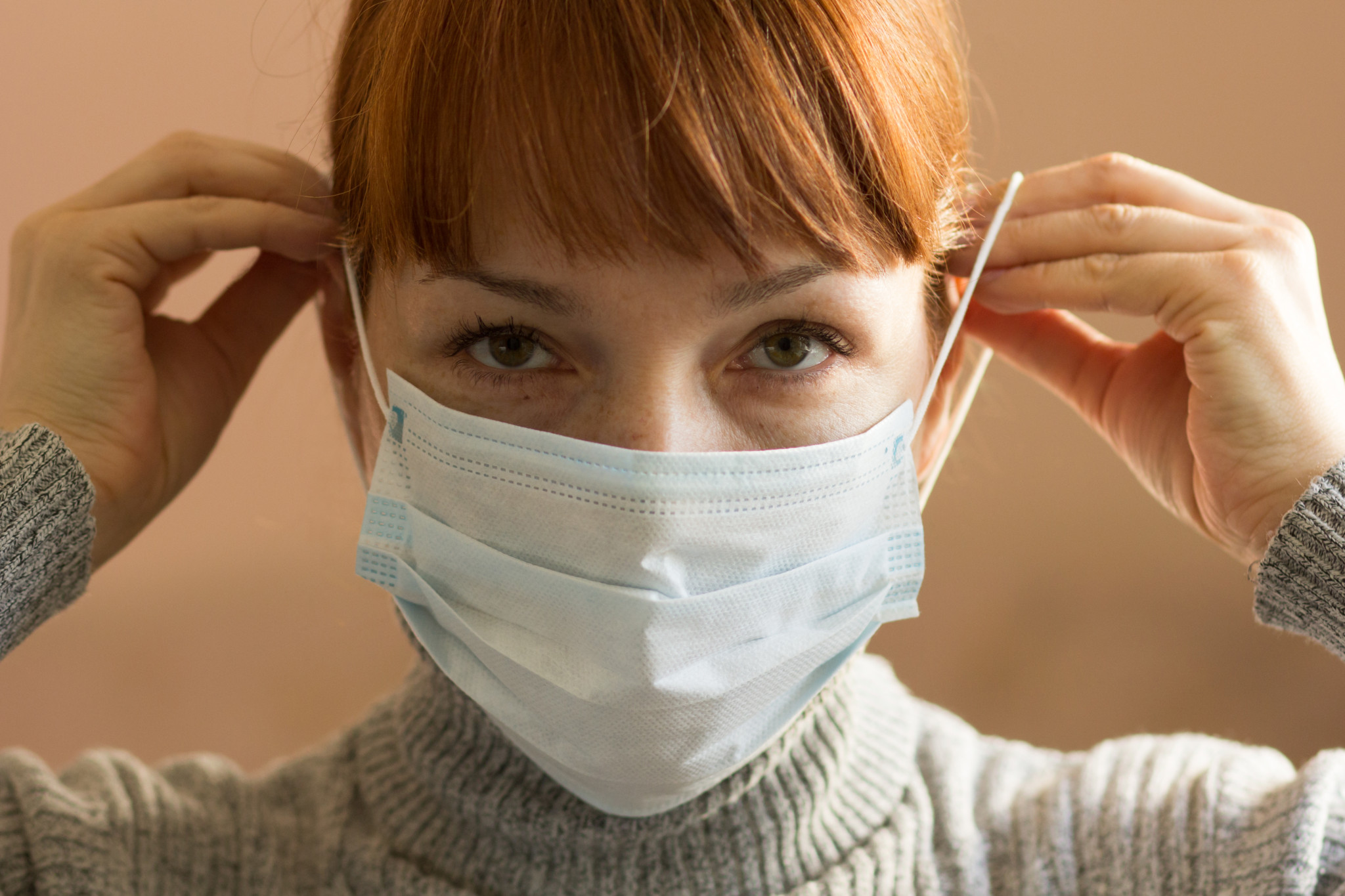 Femme d’âge moyen mettant un masque chirurgical sur son visage et regardant la caméra.