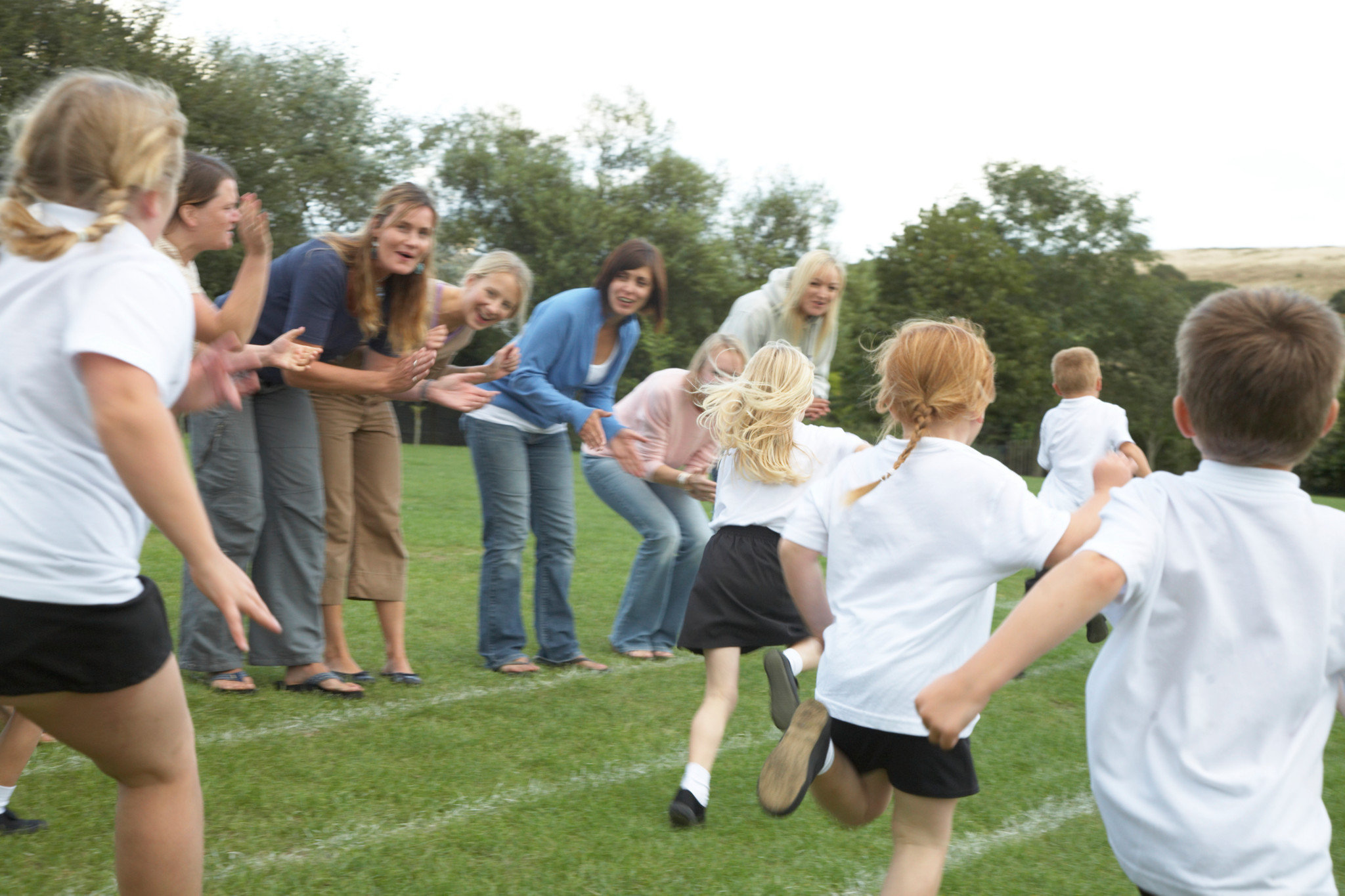 Enfants courant lors d’une course sur un terrain de sport, encouragés par des adultes applaudissant en arrière-plan.