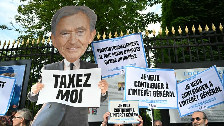 Des manifestants brandissant des pancartes, dont une à l’effigie de Bernard Arnault, lors d’une manifestation devant le Sénat, à Paris, le 12 juin 2025.