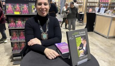 Une femme est assise à une petite table ronde avec son livre devant elle et sourit pour la photo.