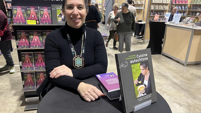 Une femme est assise à une petite table ronde avec son livre devant elle et sourit pour la photo.