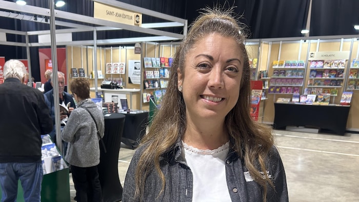 Une femme pose pour une photo. Il y a des kiosques et des étalages de livres derrière elle.