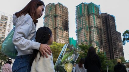 A Hong Kong, des habitants se recueillent, le 29 novembre 2025, au pied des immeubles dévastés par un incendie trois jours plus tôt. (DANIEL CENG / ANADOLU / AFP)